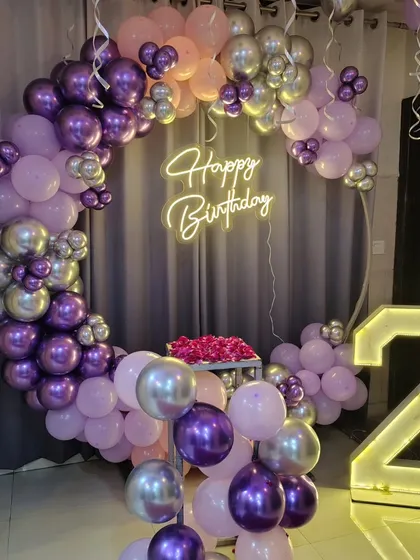A purple and silver themed birthday party, featuring a circular balloon arch, a neon sign, and a light-up number '2'.