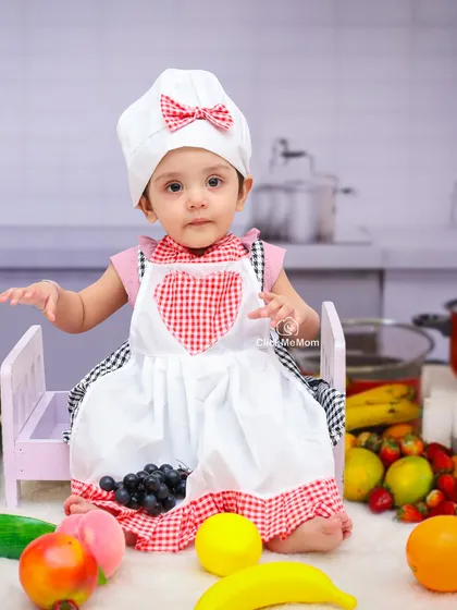 Our little chef is ready to cook up some fun. Dressed in a chef's hat and apron, she's surrounded by fresh fruits in our kitchen-themed setup.