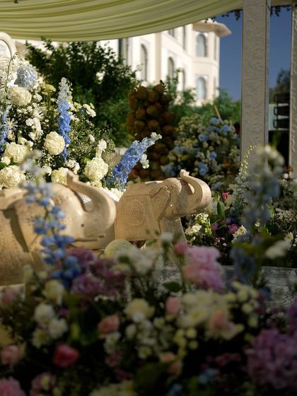 A detail from the pastel Mehendi, showing a stone elephant statue nestled within a bed of blue and white flowers.