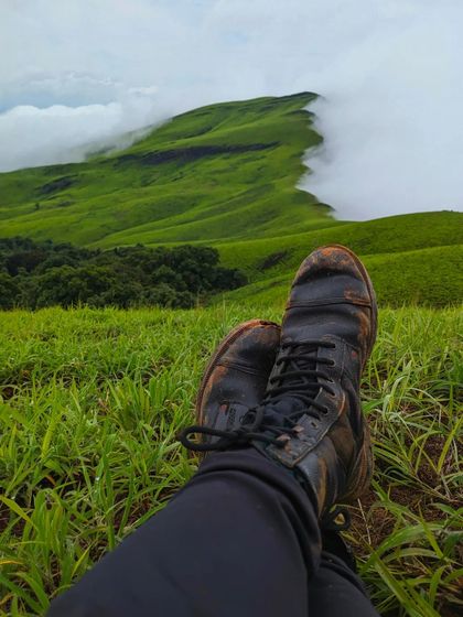 A first-person view of relaxing at Netravathi peak, with muddy boots and a stunning view.