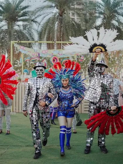 The bride makes a dazzling entry at her carnival, escorted by performers in mirrored suits and feathered headgear. Every detail is choreographed for maximum impact.