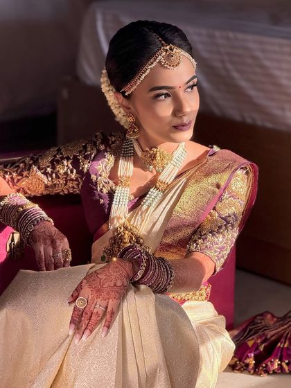 This bride is captured in the soft morning light, showing how the makeup looks natural yet defined. The look features a classic South Indian bridal hairstyle with a matha patti.