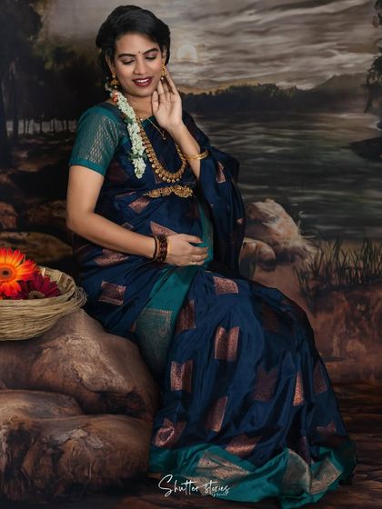 A classic and simple traditional setup. This mom-to-be is seated gracefully in a dark blue silk saree against a vintage-style painted backdrop, creating a timeless portrait.