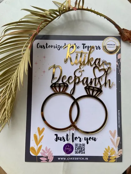 The "Ritika & Deepansh" engagement topper, shown here in its packaging, ready to add a personalized touch to their celebration.