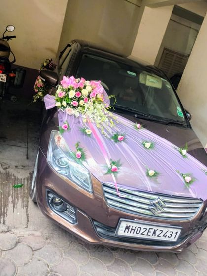 A simple and sweet car decoration. A bouquet of pink and white roses is placed on a bed of light purple fabric, with single roses dotted across the bonnet for a charming effect.