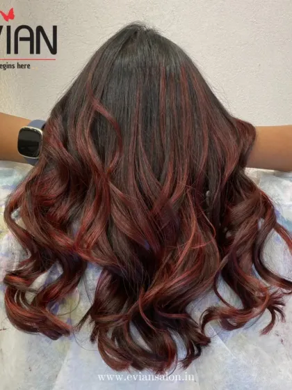 A beautiful example of red highlights woven into dark hair. The curls at the end help to blend the colors and create a seamless, fiery look.