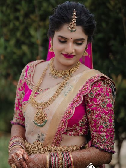 A bride in a cream and pink Kanchipuram saree with a heavily embroidered pink blouse. The floral motifs on the blouse are a beautiful example of our detailed handwork.