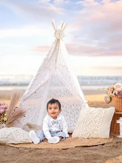 A perfect first birthday celebration against a dreamy sunset sky. Our outdoor milestone sessions combine beautiful natural light with curated props, like this boho-chic teepee setup on the beach, for stunning results.