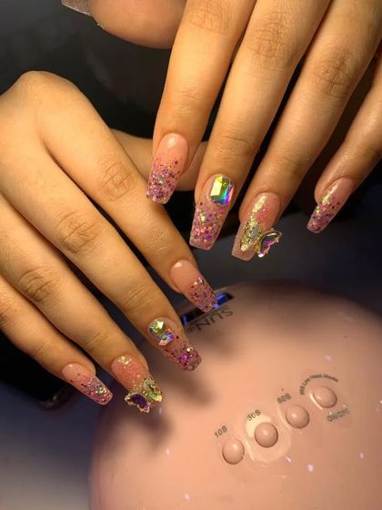 A fun and feminine set with pink glitter, 3D butterfly charms, and large iridescent crystals on long coffin-shaped extensions.