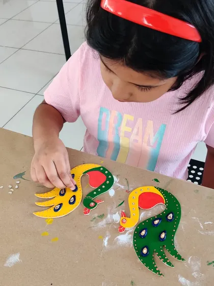 A child meticulously places small decorative elements onto her pair of peacock-shaped diya holders.