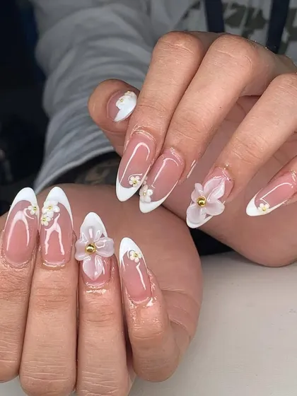 A beautiful example of 3D floral art on long stiletto nails. The classic French tips are elevated with delicate white flowers and gold bead centers.