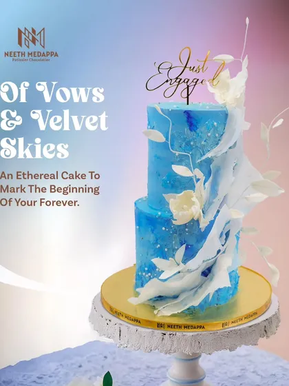 This two-tier engagement cake, titled 'Of Vows & Velvet Skies', is designed to capture the magic of new beginnings. It features a dreamy blue watercolor finish, delicate white sugar sails, and a custom 'Just Engaged' topper, making it perfect for an intimate and artistic celebration.