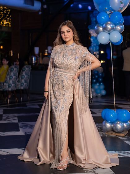 A closer look at the beige satin gown with intricate beadwork and dramatic fringe sleeves. It's a perfect statement piece for a glamorous evening.