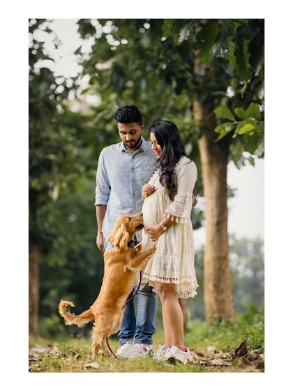 A heartwarming outdoor photo of an expecting couple with their dog, who is excitedly jumping up to greet the baby bump. It’s a perfect capture of a family growing with love.