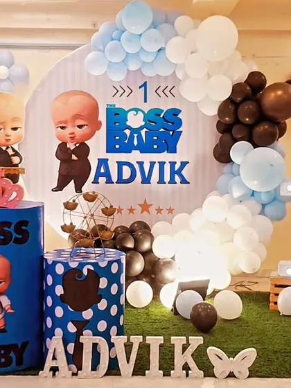 A cool Boss Baby-themed first birthday. The blue, black, and white decor features character cutouts, themed plinths, and a large light-up number '1'.