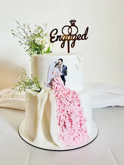 This two-tier engagement cake is all about celebrating love. I incorporated the couple's photo and created a flowing gown effect with delicate pink frosting, all finished with fresh baby's breath. It’s a perfect example of how I can personalize a cake to make your big day even more memorable.
