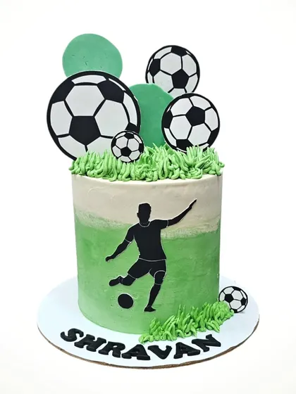 A football-themed cake with a player silhouette and soccer balls on a field of green buttercream.
