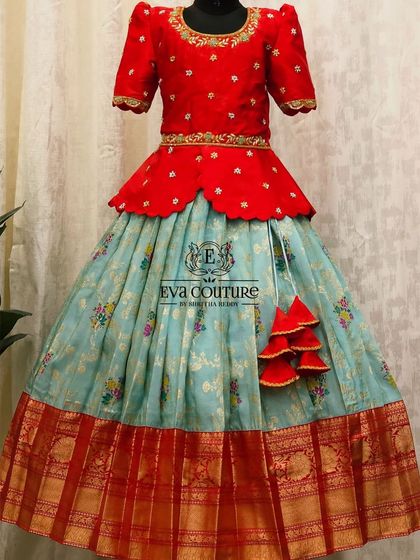 A lovely combination of red and pastel blue. This peplum Pattu Pavadai features a floral printed skirt with a traditional red and gold border.