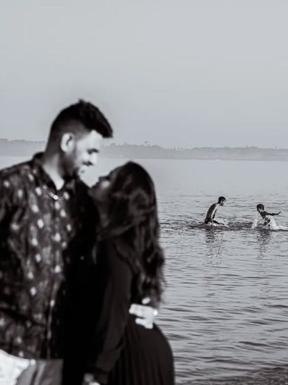 A candid moment of Manoj and Jagruti by the sea, with other beachgoers in the background. This photo captures the real, unscripted environment of a public location shoot.