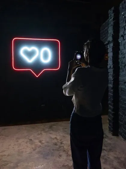 Another angle of a person engaging with the 'Heart 0' neon sign. The dark, industrial setting of the gallery space enhances the impact of the glowing light.