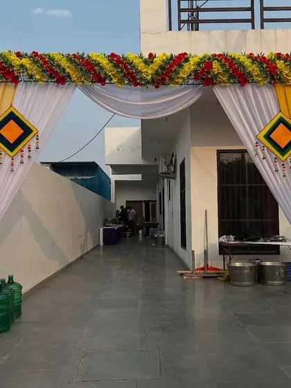 A daytime entrance arch for a home function, decorated with yellow and white drapes and a floral border.