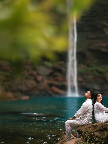 Sitting back to back on a rock, gazing peacefully at the waterfall. This pose suggests a comfortable, easy companionship and a shared appreciation for the beauty around them.