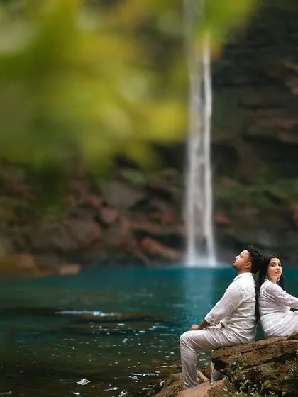 Sitting back to back on a rock, gazing peacefully at the waterfall. This pose suggests a comfortable, easy companionship and a shared appreciation for the beauty around them.