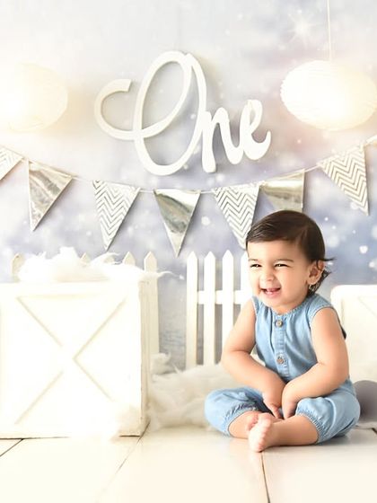 A happy smile in a winter-themed first birthday setting. The clean, bright setup with a simple "One" sign keeps the focus on the birthday boy.