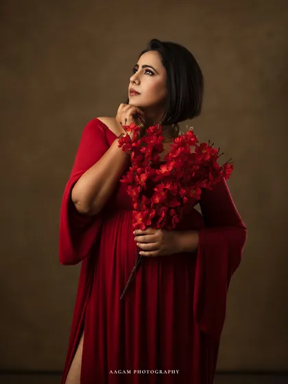 Looking upwards, she holds a bouquet of red flowers, creating a sense of drama and aspiration.
