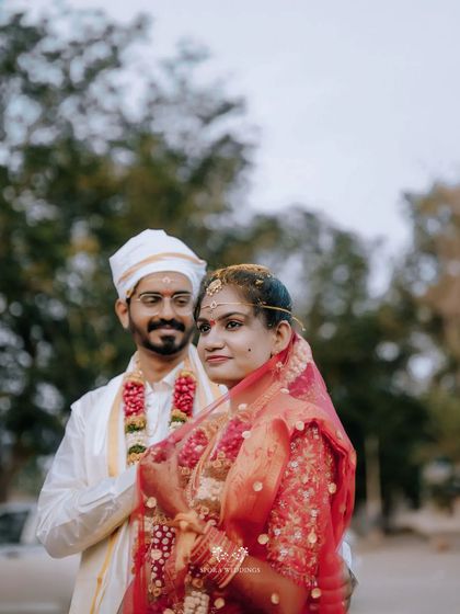 A portrait of the couple outdoors, the groom looking lovingly at his bride in her beautiful red wedding saree.