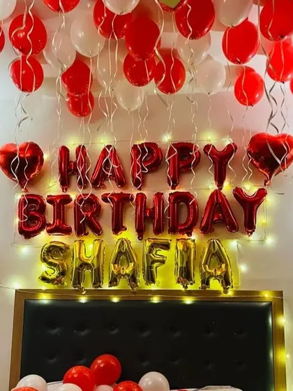 I can personalize your birthday decorations with a name, like this 'SHAFIA' foil balloon setup. The 'Happy Birthday' letters are complemented by the name in gold, with red and white balloons filling the room.