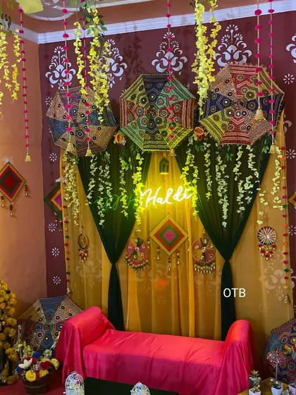 This Haldi backdrop combines traditional elements like Rajasthani umbrellas and wall stencils with a modern neon sign. The dark green and yellow drapes create a rich, festive look.