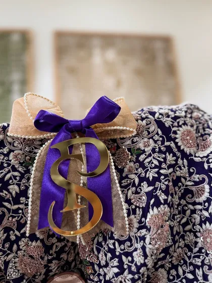 The rich texture of this navy blue embroidered blouse is complemented by a royal purple ribbon and a custom initial tag.