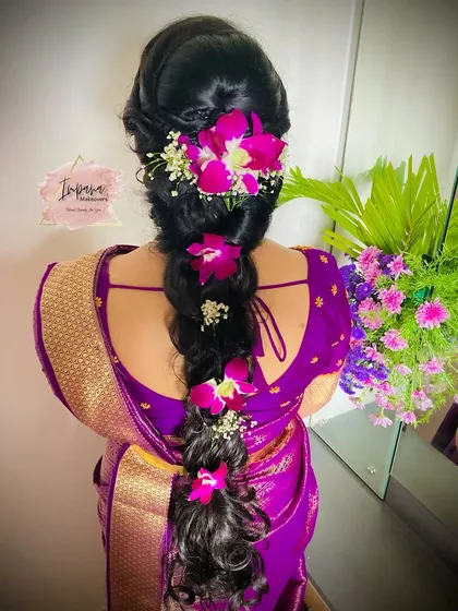 A modern take on a traditional hairstyle. This messy braid, decorated with fresh orchids, is perfect for a housewarming or a pre-wedding event, offering a chic yet elegant look.