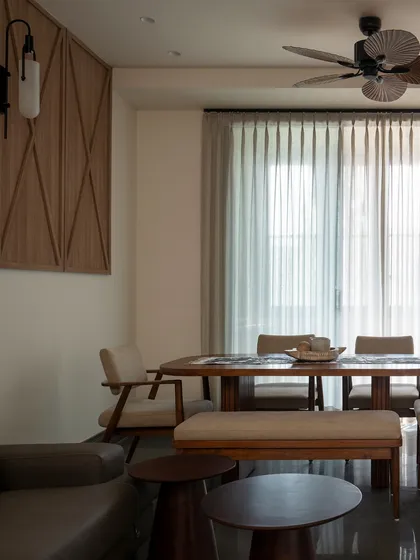 The dining area is part of an open, continuous layout. The custom teakwood table with its fluted base is surrounded by soft textures and neutral tones, creating a space that is grounded and adaptable.