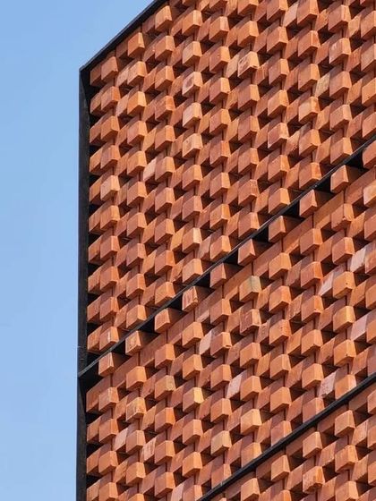 A close-up detail of the 'Ishtika' brick facade, showing the texture and pattern of the sand-toned bricks against a clear blue sky.