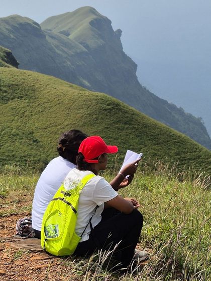 Two trekkers taking a break to read on the trail, with the stunning Bandaje landscape as their backdrop.