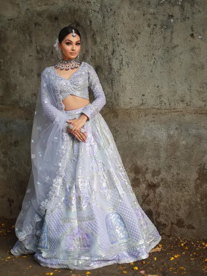 A model posing against a rustic wall in the lavender lehenga, showing how the outfit stands out in any setting.