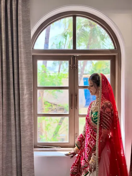 A beautifully composed shot of the bride by the window. The natural light highlights the soft, dewy finish of her skin.