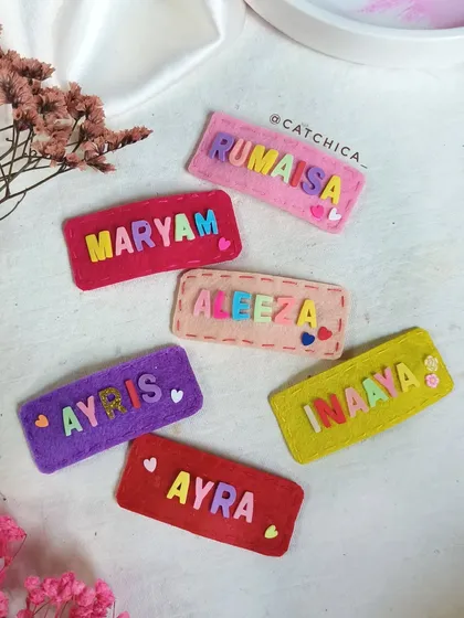 A colorful collection of our 'Name Fusion' felt clips. Each one is hand-stitched with care, featuring names like 'Rumaisa', 'Maryam', and 'Inaaya'.