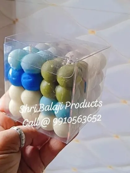 A hand holding a 3-inch cube PVC box with a colorful bubble candle inside. The crystal clear packaging really lets the product shine.