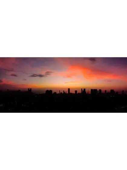 A wide panoramic view of the silhouetted Mumbai skyline under a dramatic, colorful sunset.