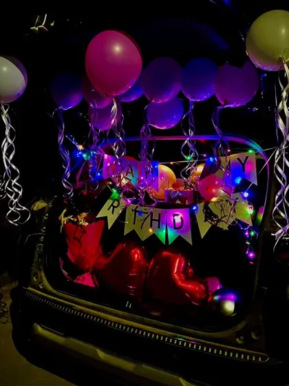 A car trunk decoration at night. The fairy lights and heart-shaped balloons create a magical glow, making for a very memorable birthday surprise.