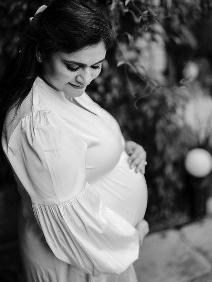 A classic black and white portrait focusing on the beautiful curve of the baby bump. The mom-to-be looks down with a loving expression.