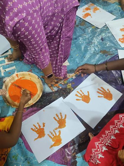 A top-down view of the handprint painting station. The bright orange paint and focused hands show the sensory joy of this activity.