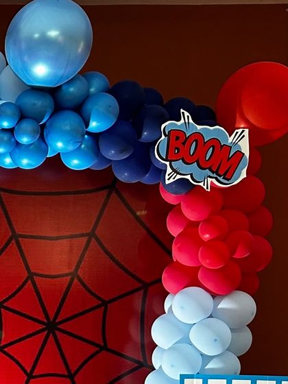 A "BOOM!" graphic adds a punch of fun to this red, white, and blue balloon arch for a superhero-themed event.