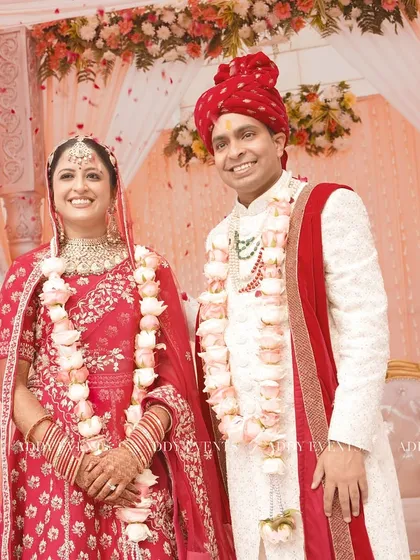 The newly married couple shares a happy moment under their beautiful peach-toned floral mandap, with petals showering down on them.