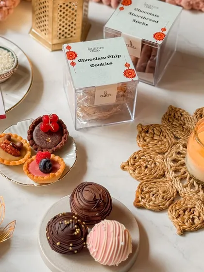 A beautiful arrangement of Rakhi treats, including mini tarts, chocolate bombs, and boxes of cookies and shortbread sticks. This shows how you can create a custom gift hamper with my individual items.