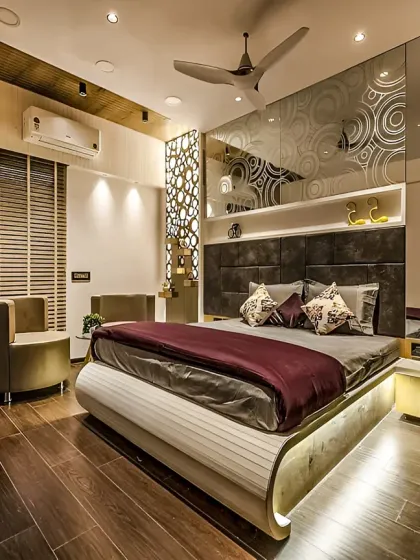 In this luxurious master bedroom, we layered multiple lighting sources, including track lights and backlit panels, to create a warm and inviting ambiance. The design combines a uniquely curved bed frame with intricate wall details and rich wood flooring for a truly opulent feel.