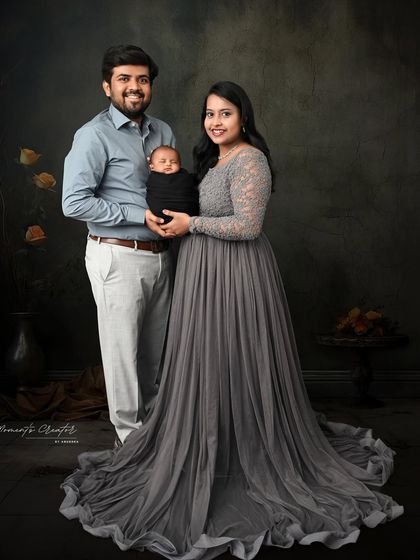A simple and elegant family portrait. The parents hold their newborn, dressed in coordinated grey tones that create a soft and harmonious image.